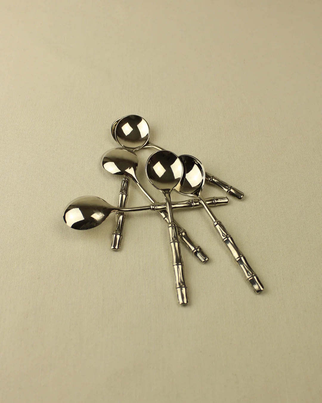Five Bamboo Silver-Plated Spoons of varying sizes lying on a beige surface, positioned randomly with reflections visible on the spoons from Boga Avante Shop.