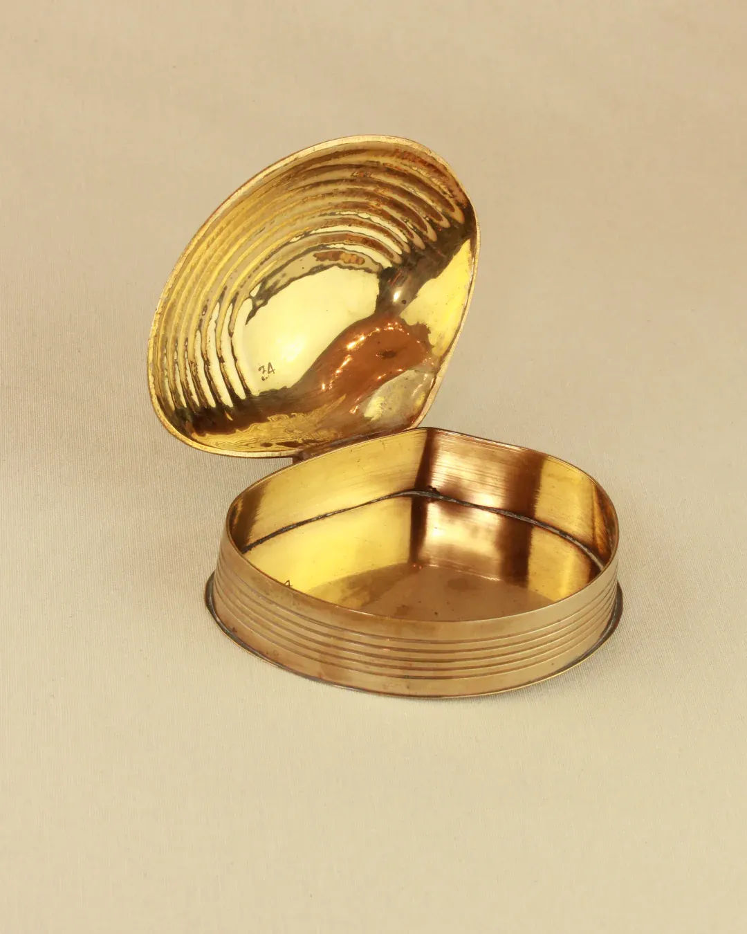 An open Boga Avante Shop brass shell dish, with a reflective interior in the lid and a compartment in the base, set against a neutral background. This brass-hinged treasure resembles an antique jewellery box.