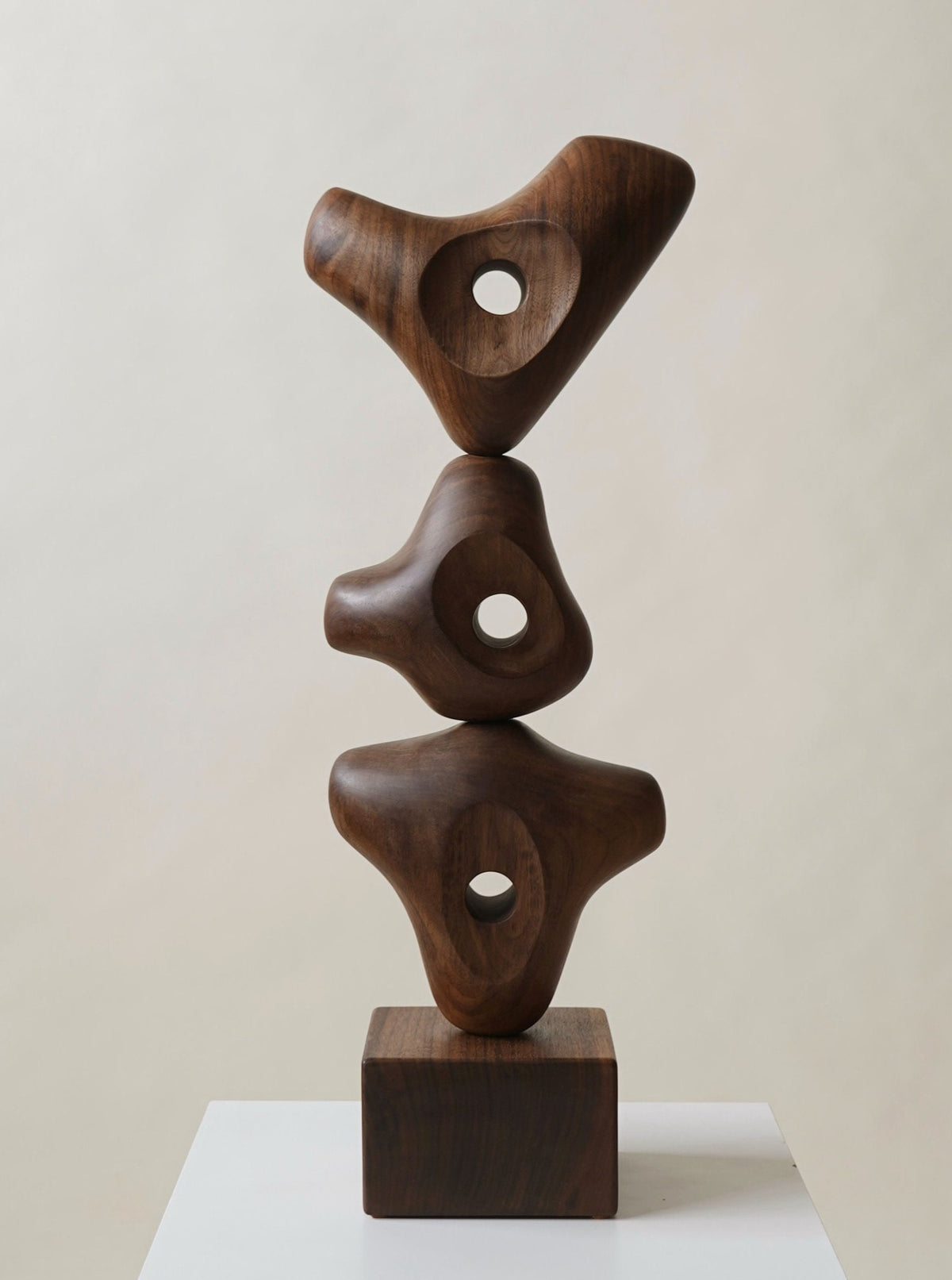 A modern Juok Sculpture by Chandler McLellan consisting of three abstract forms, each with a central hole, stacked on top of each other and mounted on a square base, displayed against a neutral background.