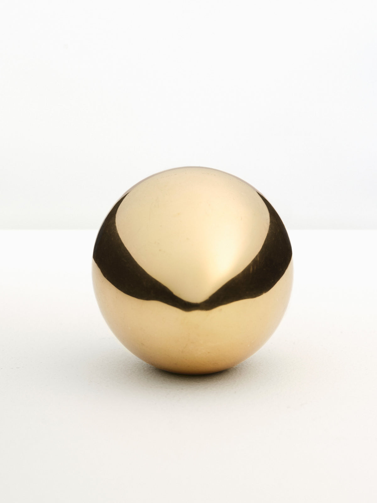 A golden sphere with a matte finish and a black horizontal stripe around its center, set against a white background, serves as an elegant Fourth St brass egg paperweight.