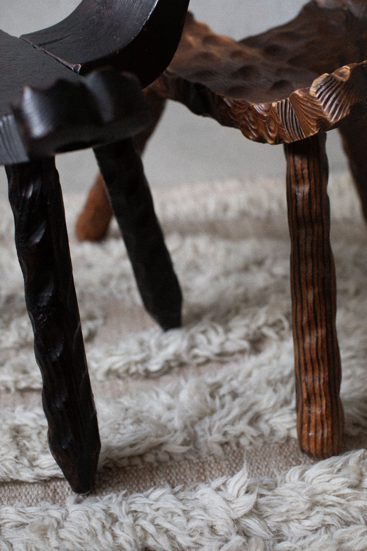 Close-up view of an intricately carved brown wood Brutalist Chair by Out For Lunch on a shaggy white rug, featuring a detailed texture on the legs and a smooth, wavy seat design.