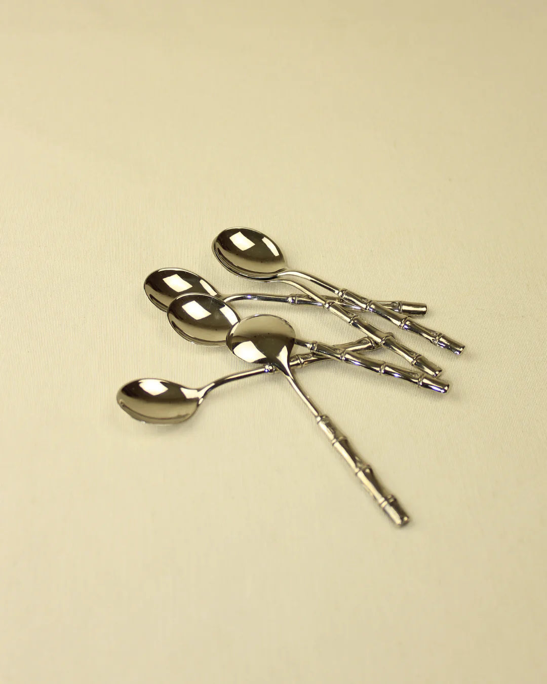 A set of four Bamboo Silver-Plated Spoons from Boga Avante Shop, with intricate handles, arranged on a light beige surface.