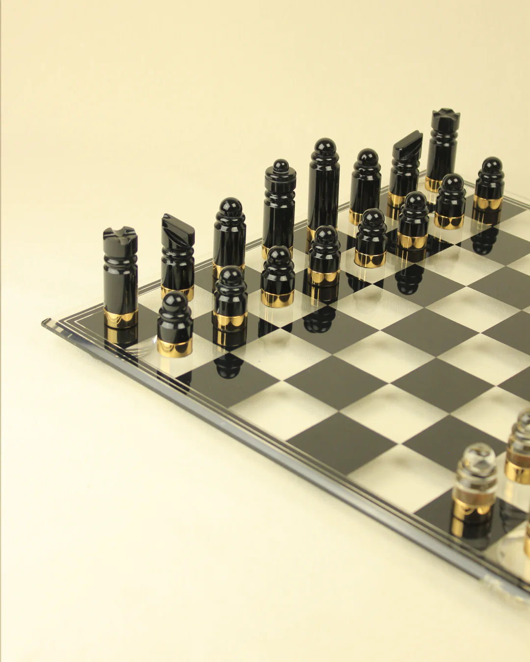 A sleek Boga Avante Shop glass Chess & Checker Board with black and clear glass pieces arranged for a game, featuring brass accents, set against a light beige background.