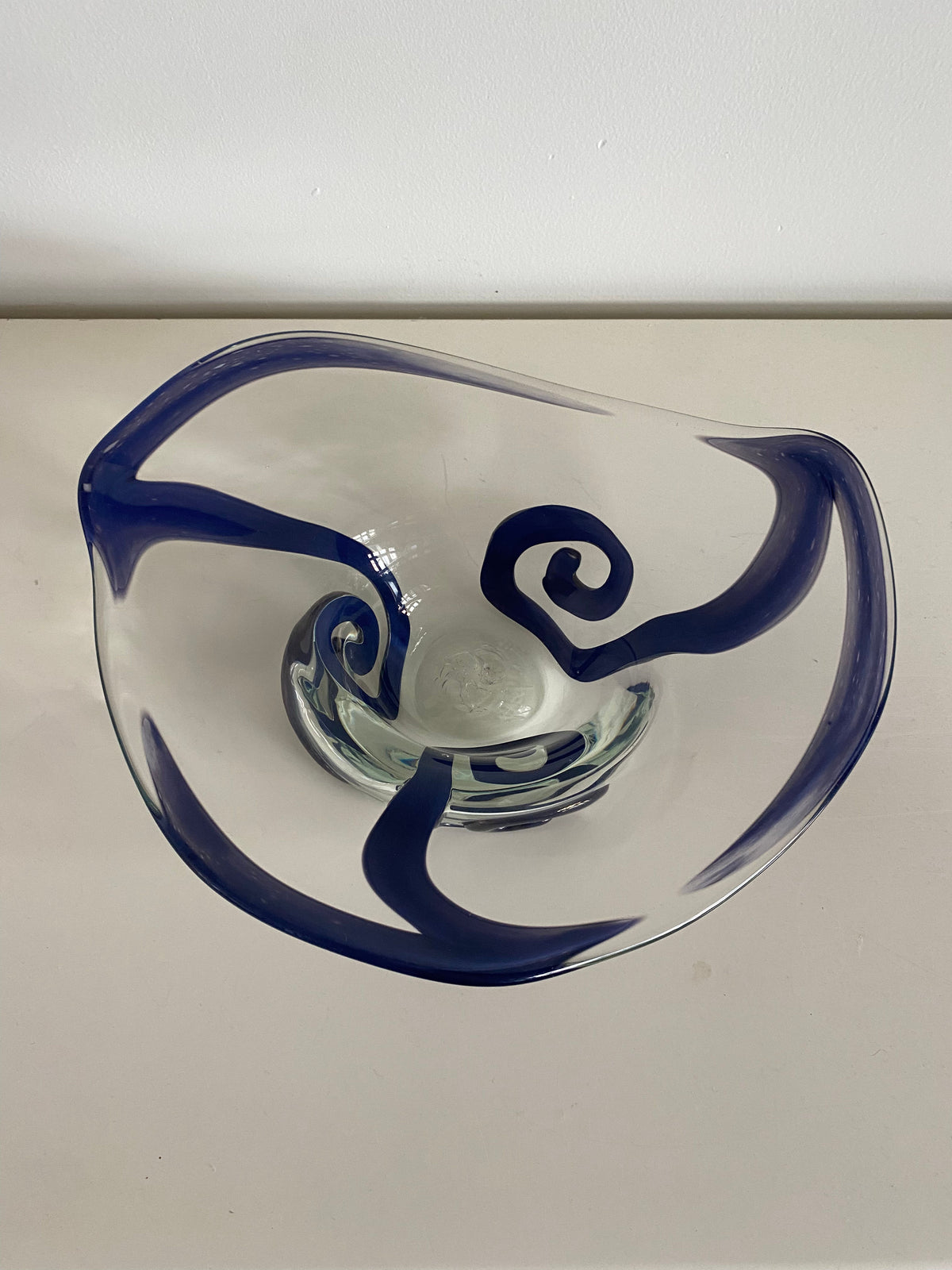 A clear Les Objets Amsterdam vintage glass bowl featuring exquisite craftsmanship, with stylish, swirling blue designs on a white surface.