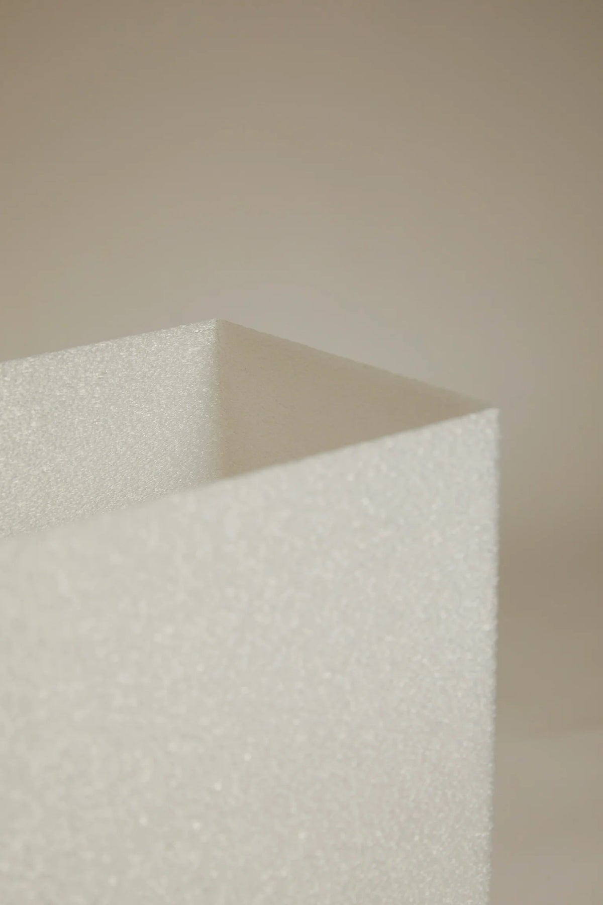 A close-up of Lampe i by Argot Studio, a textured, white sculptural object with sharp edges and a slightly sparkly surface, set against a beige background. It embodies minimalist aesthetics perfect for luxury interior design.