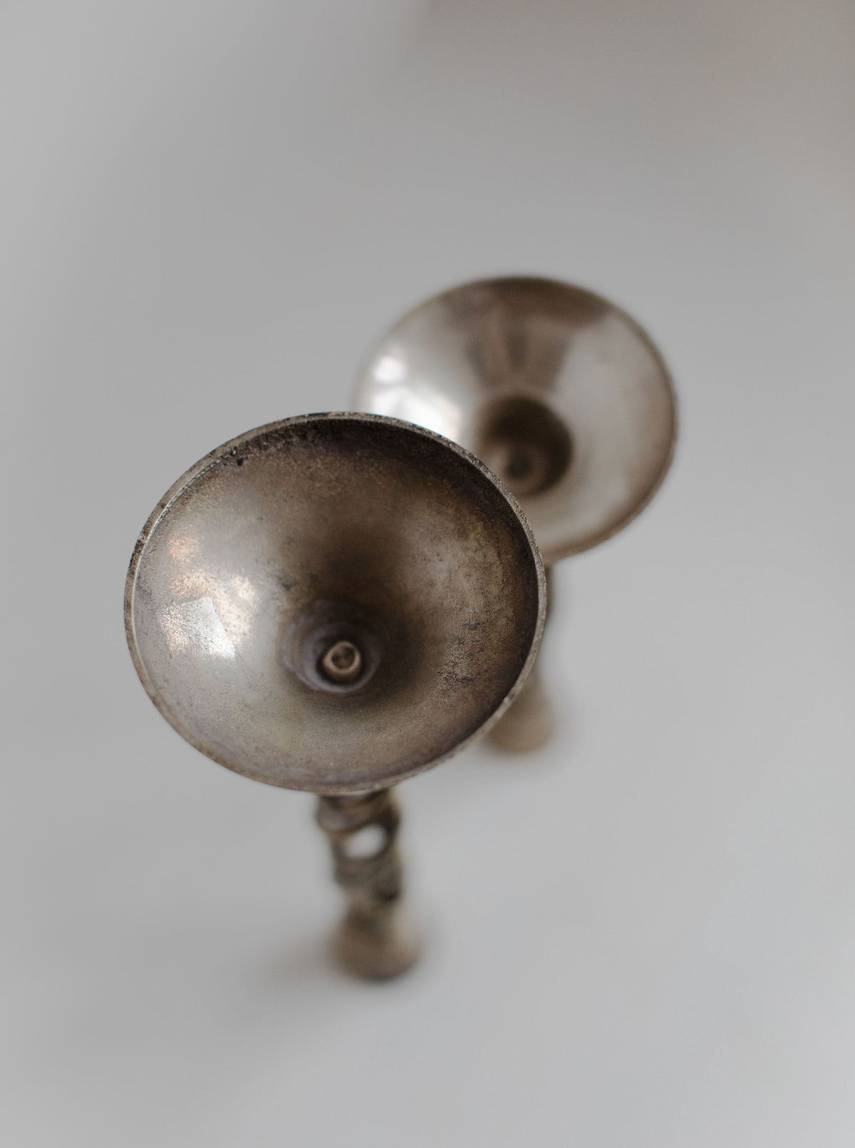 Two Out For Lunch Brass Twisted Candleholders with a tarnished surface, shown up close against a soft white background, focusing on their circular, cup-like tops to highlight their vintage charm.