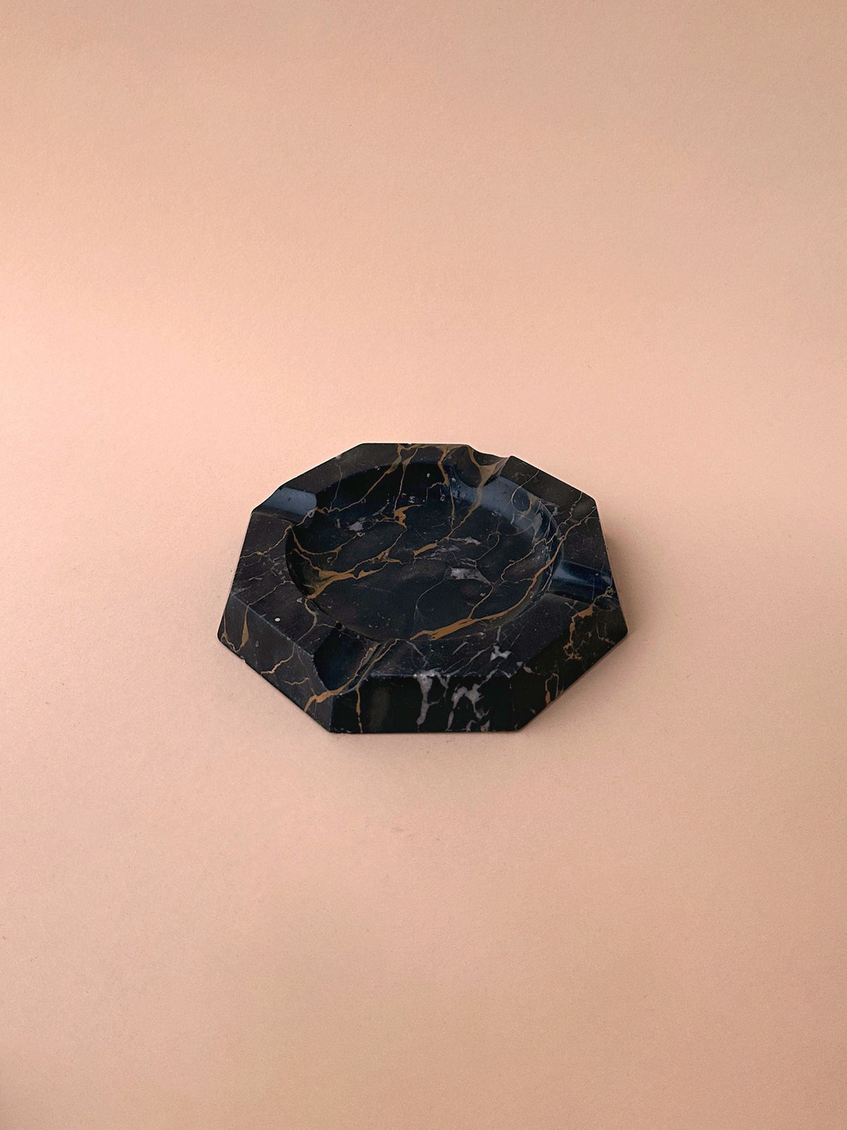 An octagonal 1970s Dodo Vintage black marble ashtray with white and gold veins on a beige background.