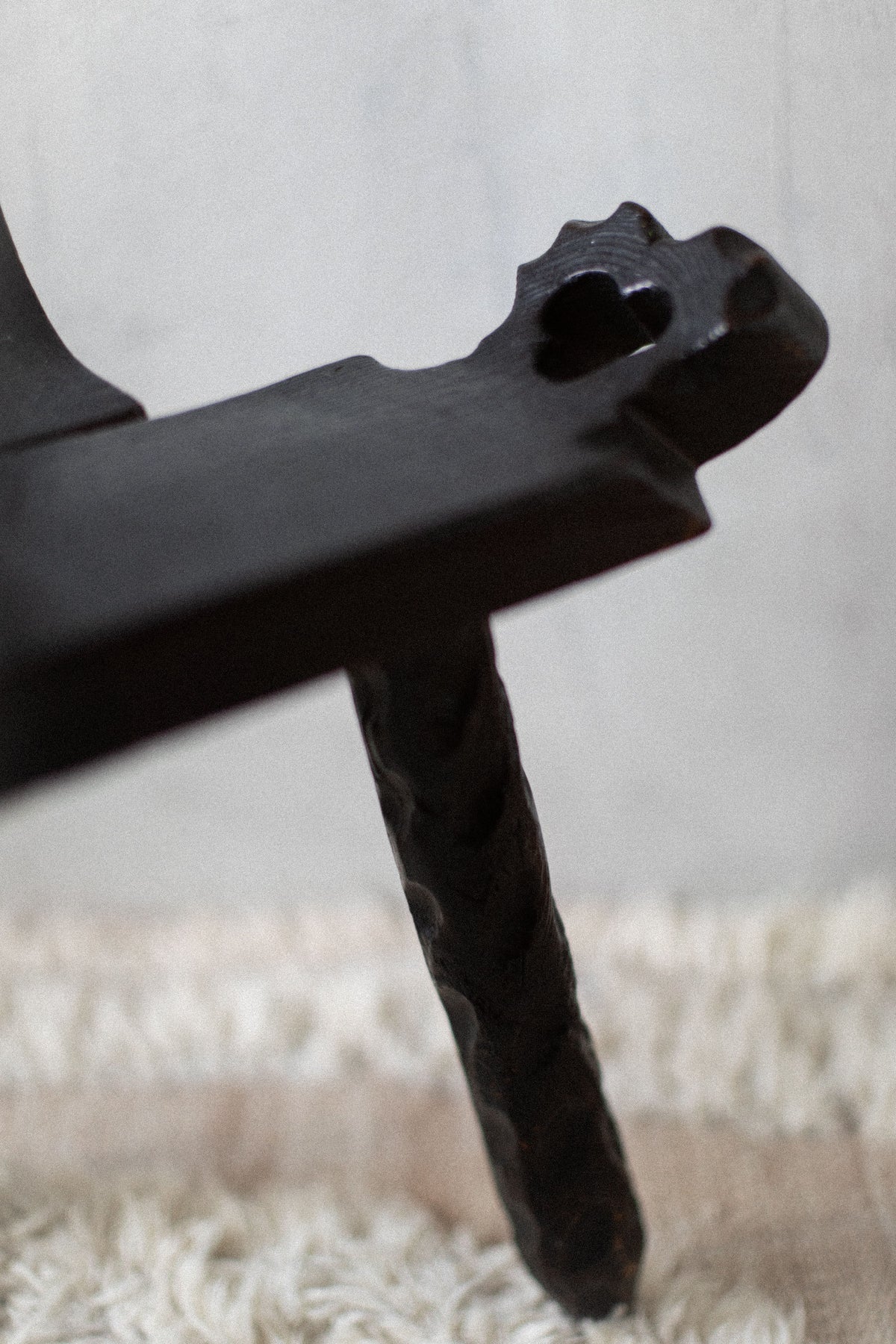 Close-up of a black wrought iron candle holder with an intricate twisted handle and a Brutalist Chair design, set against a softly textured cream background by Out For Lunch.